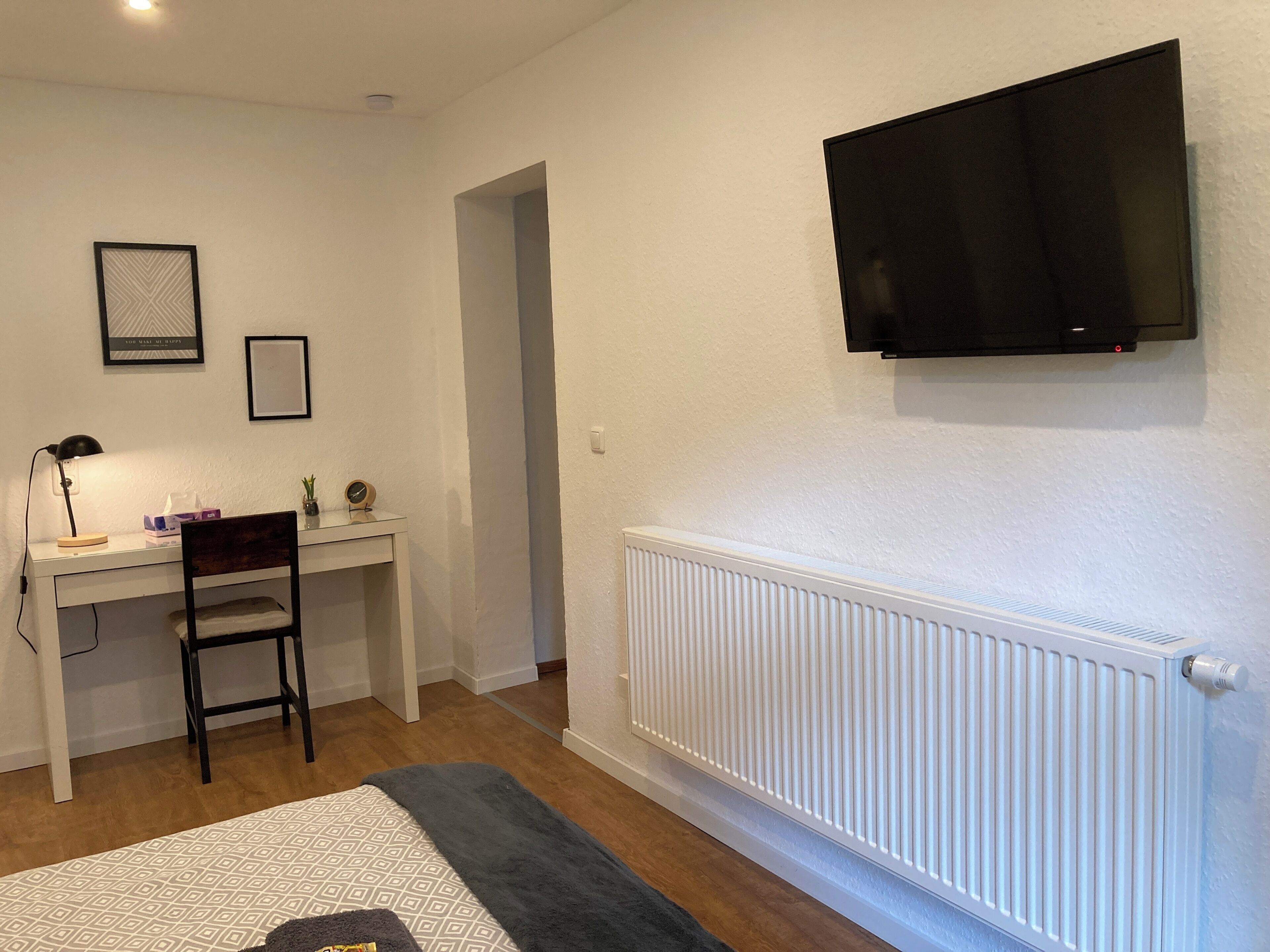 A room with a desk, chair, TV, and radiator.