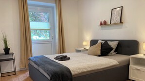 Ein modernes Schlafzimmer mit einem Bett, Nachttischen, einer Zimmerpflanze und einem Fenster mit Vorhängen.