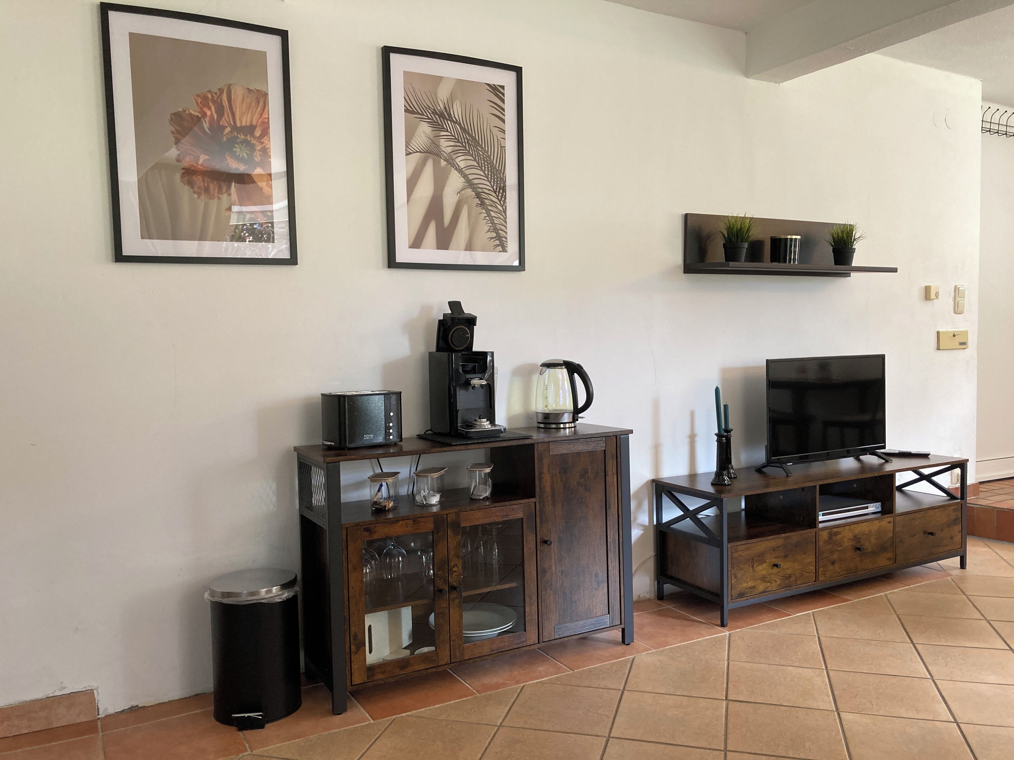 Un salon équipé d’une machine à café, d’un téléviseur et d’œuvres d’art encadrées accrochées au mur.