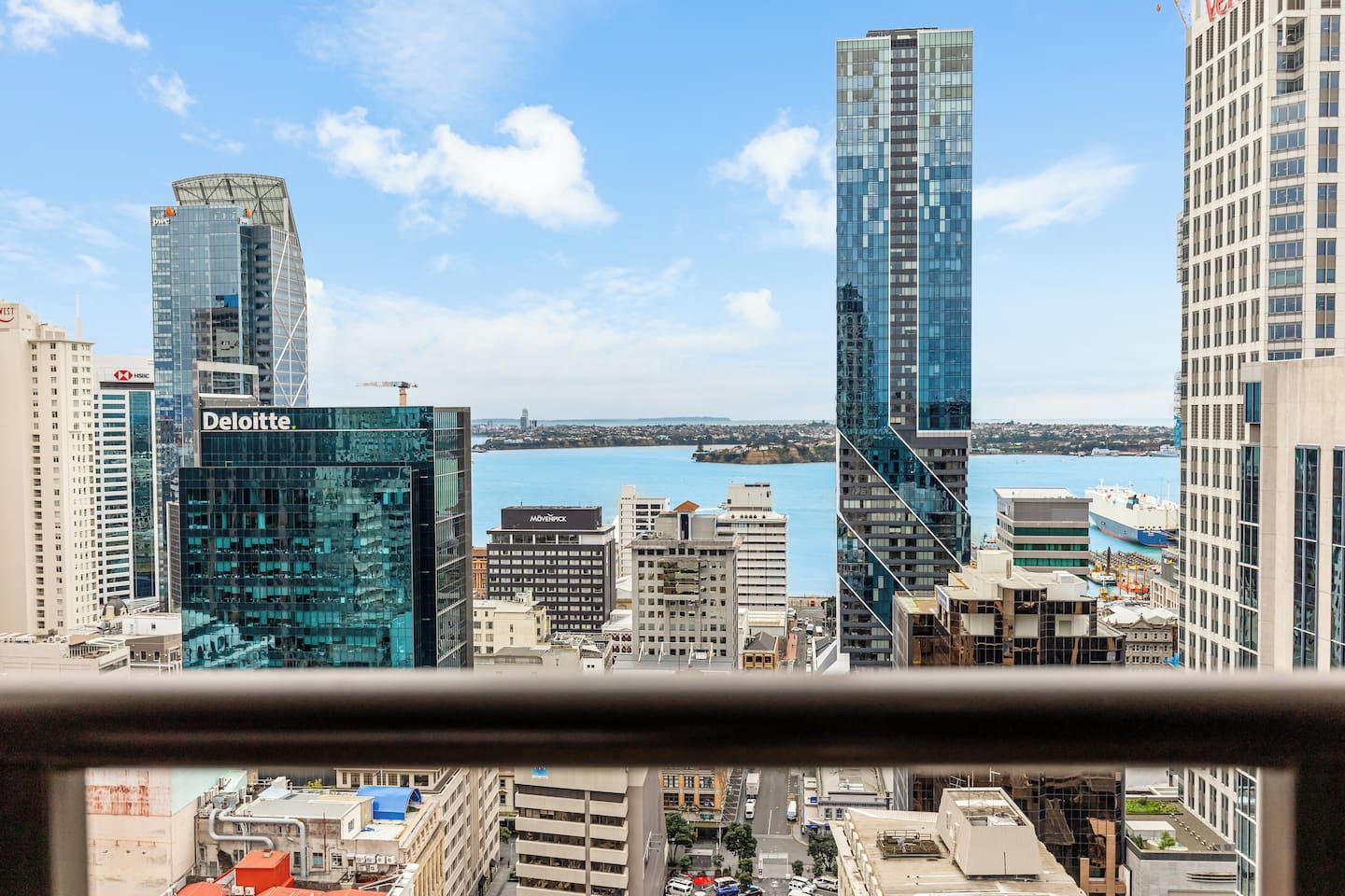 Un paysage urbain avec des immeubles modernes de grande hauteur, dont un bâtiment emblématique de Deloitte, et une vue sur le front de mer.