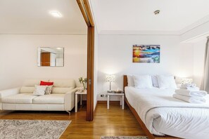 Ein Hotelzimmer mit Bett, Sofa, Nachttisch, Lampe, Gemälde und Spiegel.