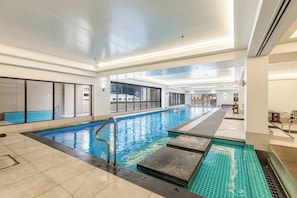 An indoor swimming pool with clear water, a diving board, and a tiled floor.