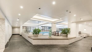 Un hall d’entrée spacieux avec un plafond haut, des luminaires encastrés et un espace salon central agrémenté de plantes en pot.
