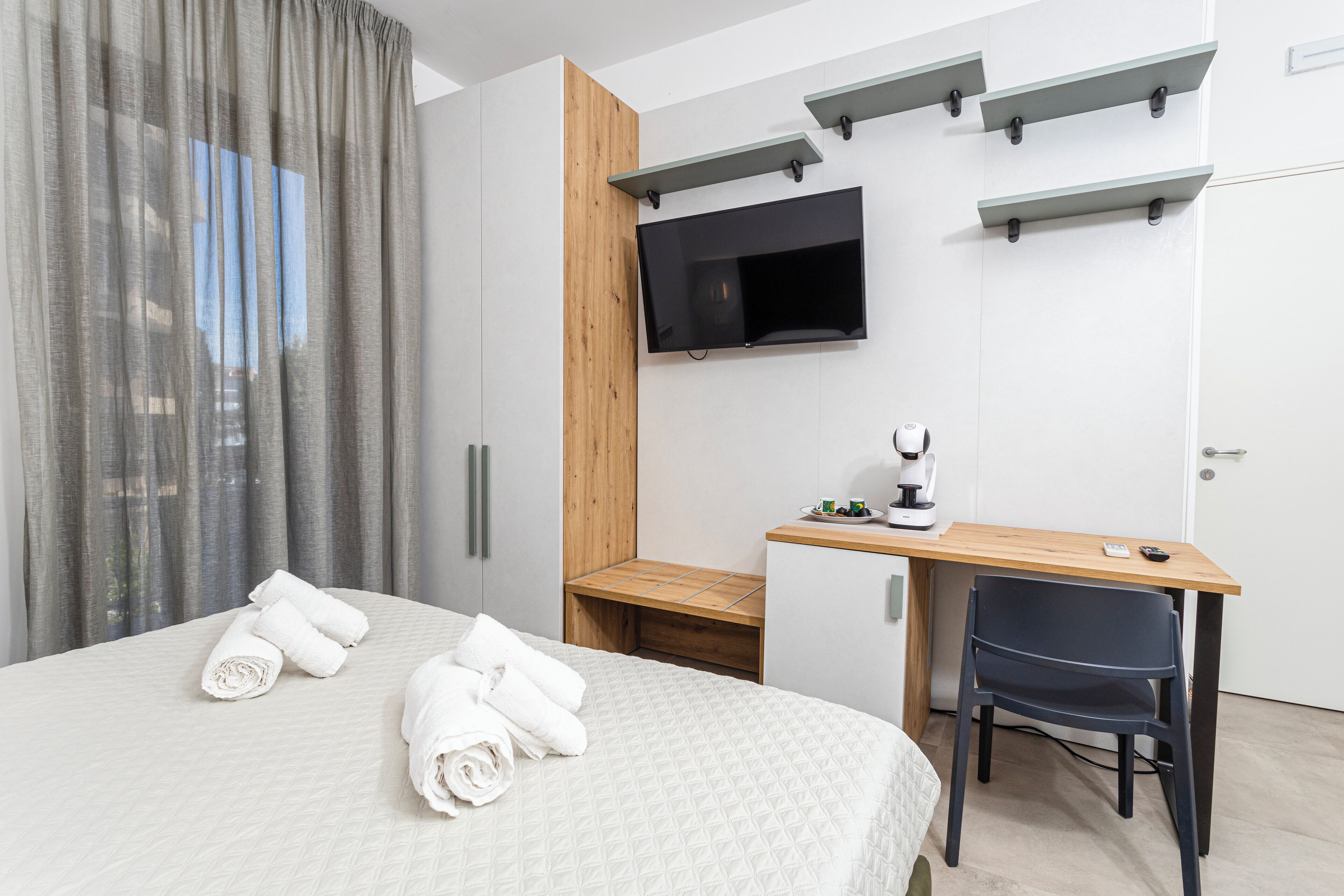 Habitació d'hotel moderna amb un llit, un escriptori, una cadira, un televisor muntat a la paret i un element decoratiu de fusta.