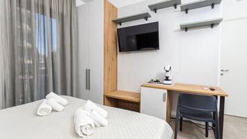 Habitació d'hotel moderna amb un llit, un escriptori, una cadira, un televisor muntat a la paret i un element decoratiu de fusta.