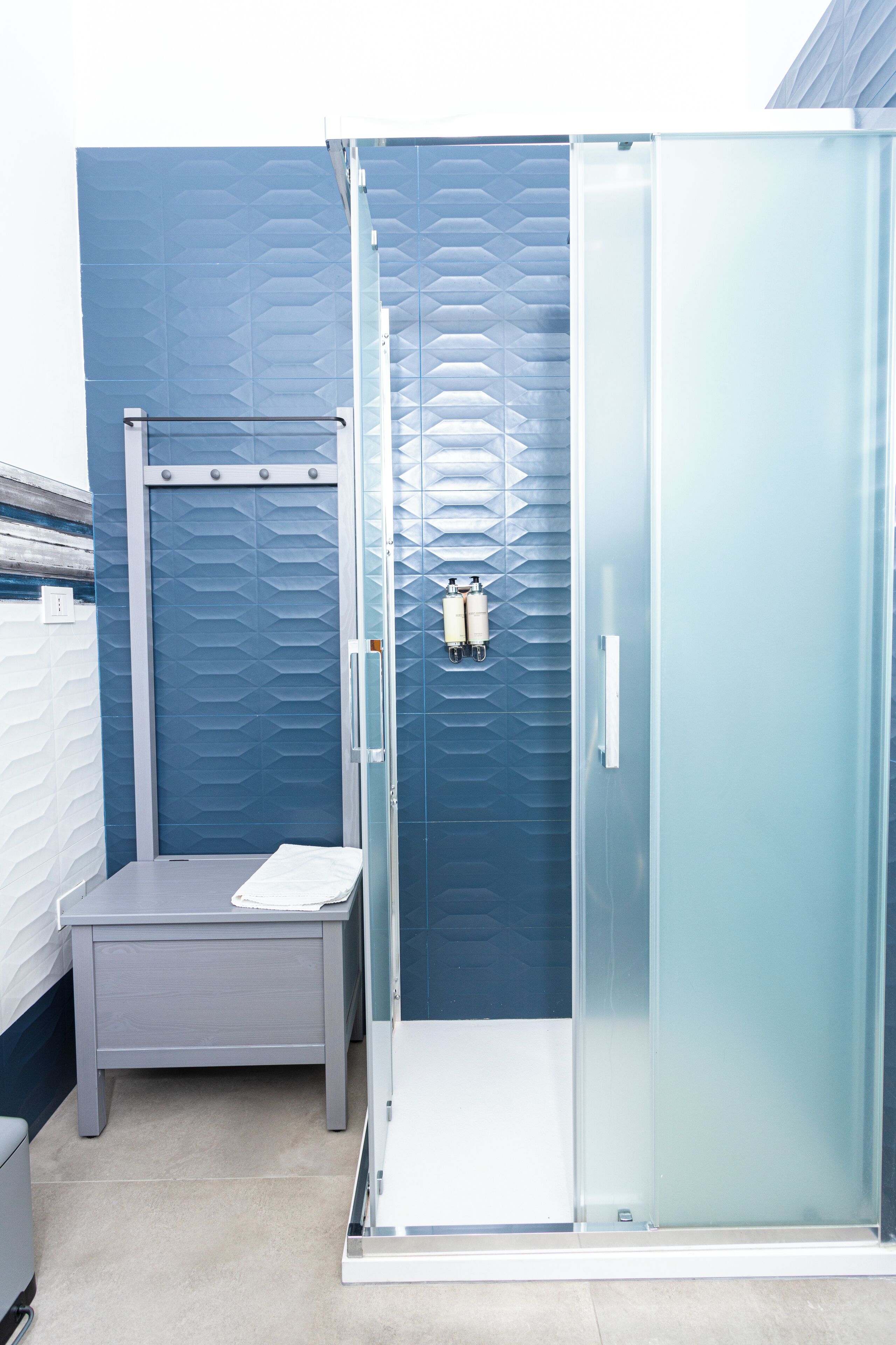 Un baño moderno con cabina de ducha, un banco y un perchero para toallas.