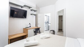 A modern hotel room with a large bed, a desk with a chair, a television mounted on the wall, and a shower area visible through an open door. - Gallo's City Rooms (Termoli)