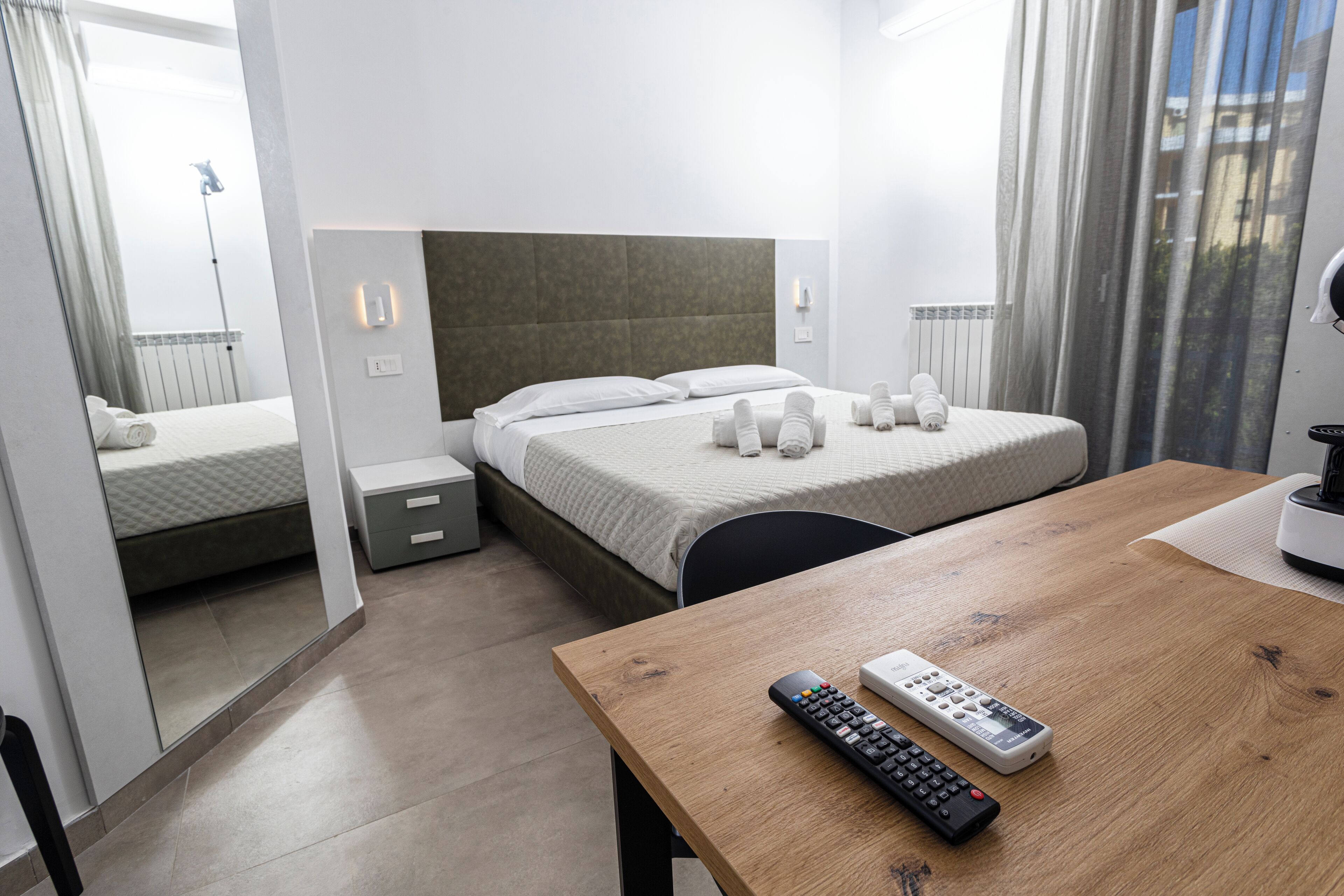 Una habitación de hotel con cama, mesitas de noche, una mesa de madera y un control remoto.