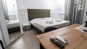Una habitación de hotel con cama, mesitas de noche, una mesa de madera y un control remoto.