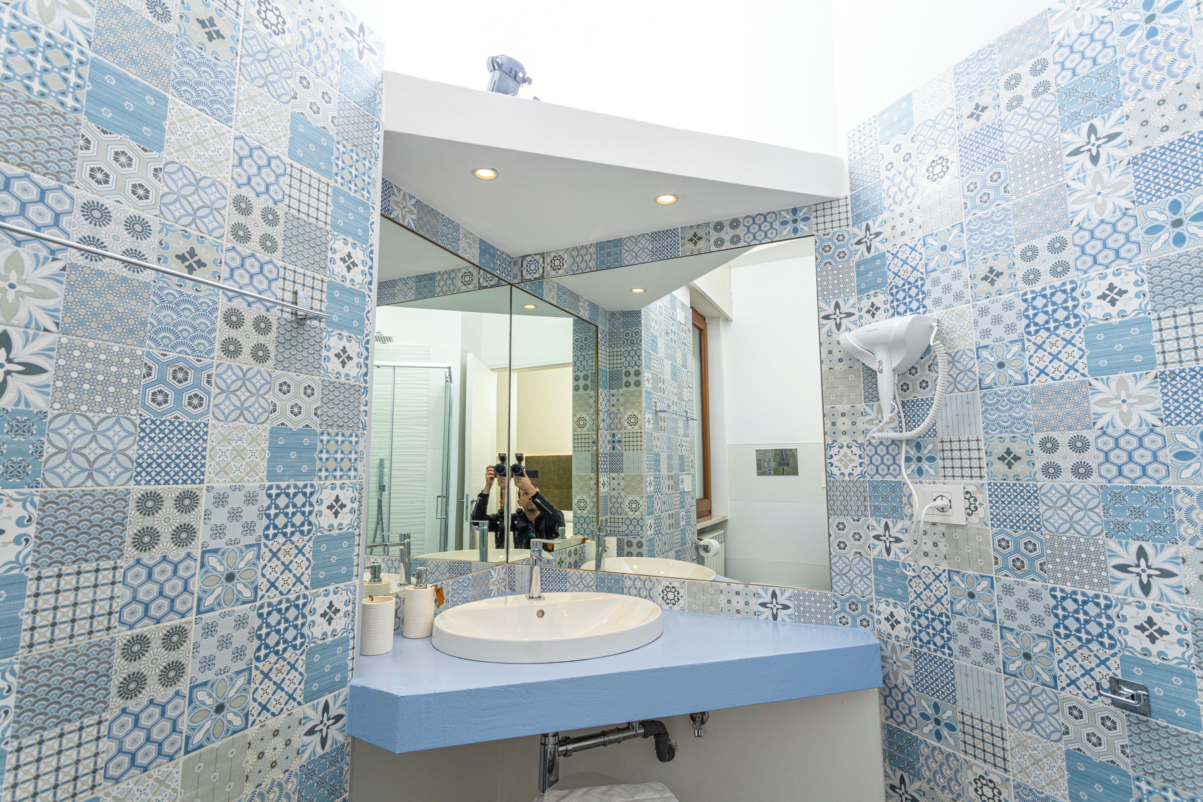 Un baño con pared de azulejos blancos y azules, un lavabo blanco y un espejo.