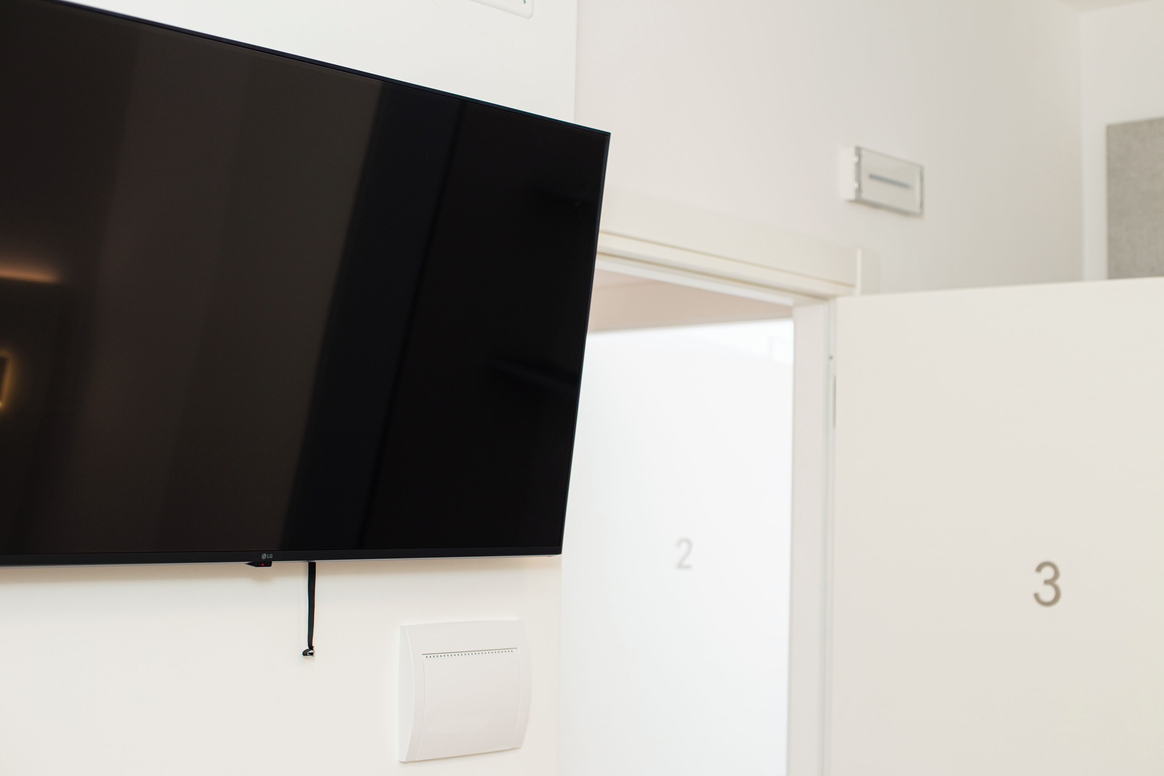 Ein modernes Hotelzimmer mit einem an der Wand befestigten Flachbildfernseher, einem Thermostat und nummerierten Türen.
