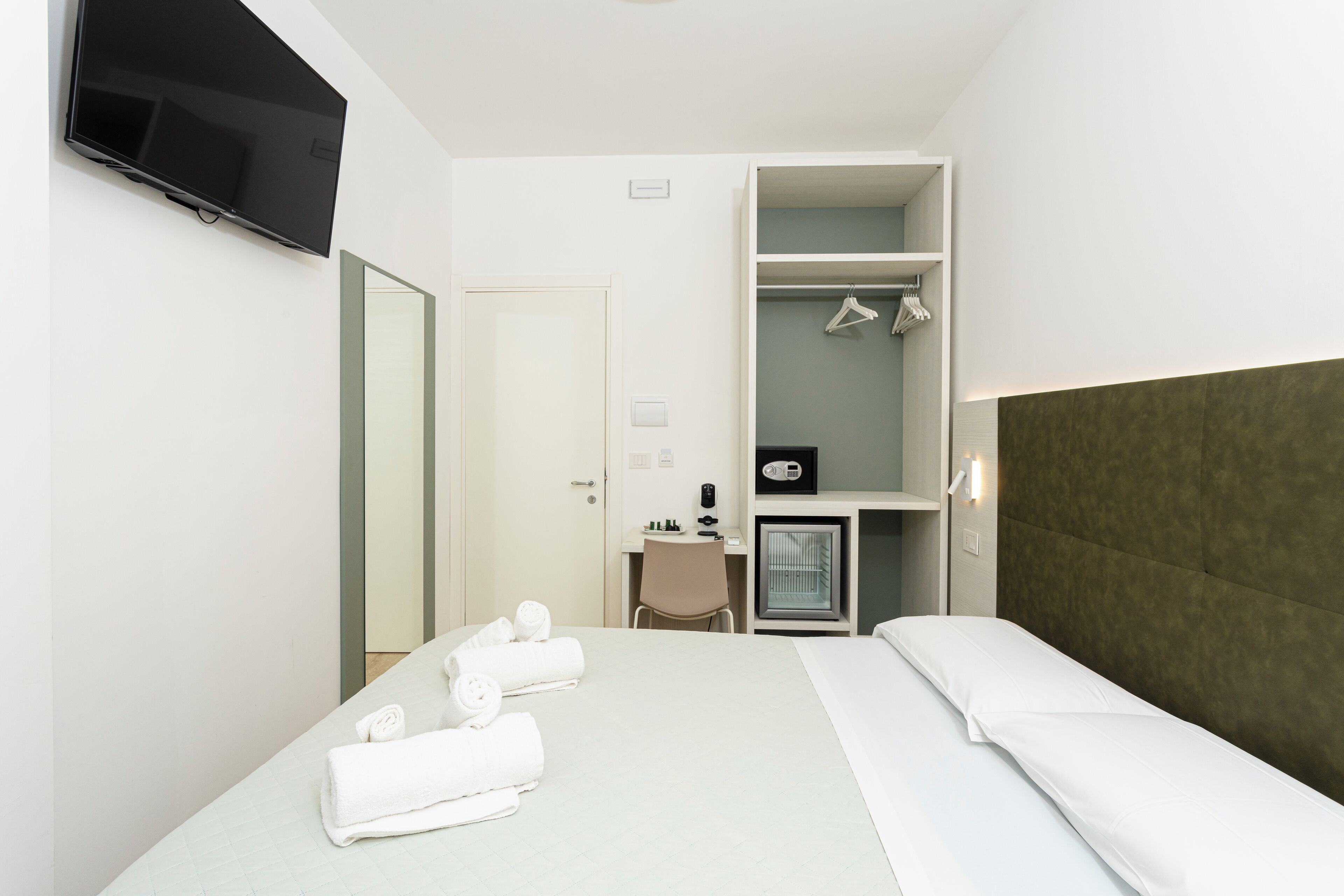 A hotel room with a bed, a desk, a chair, a TV, and a wardrobe.