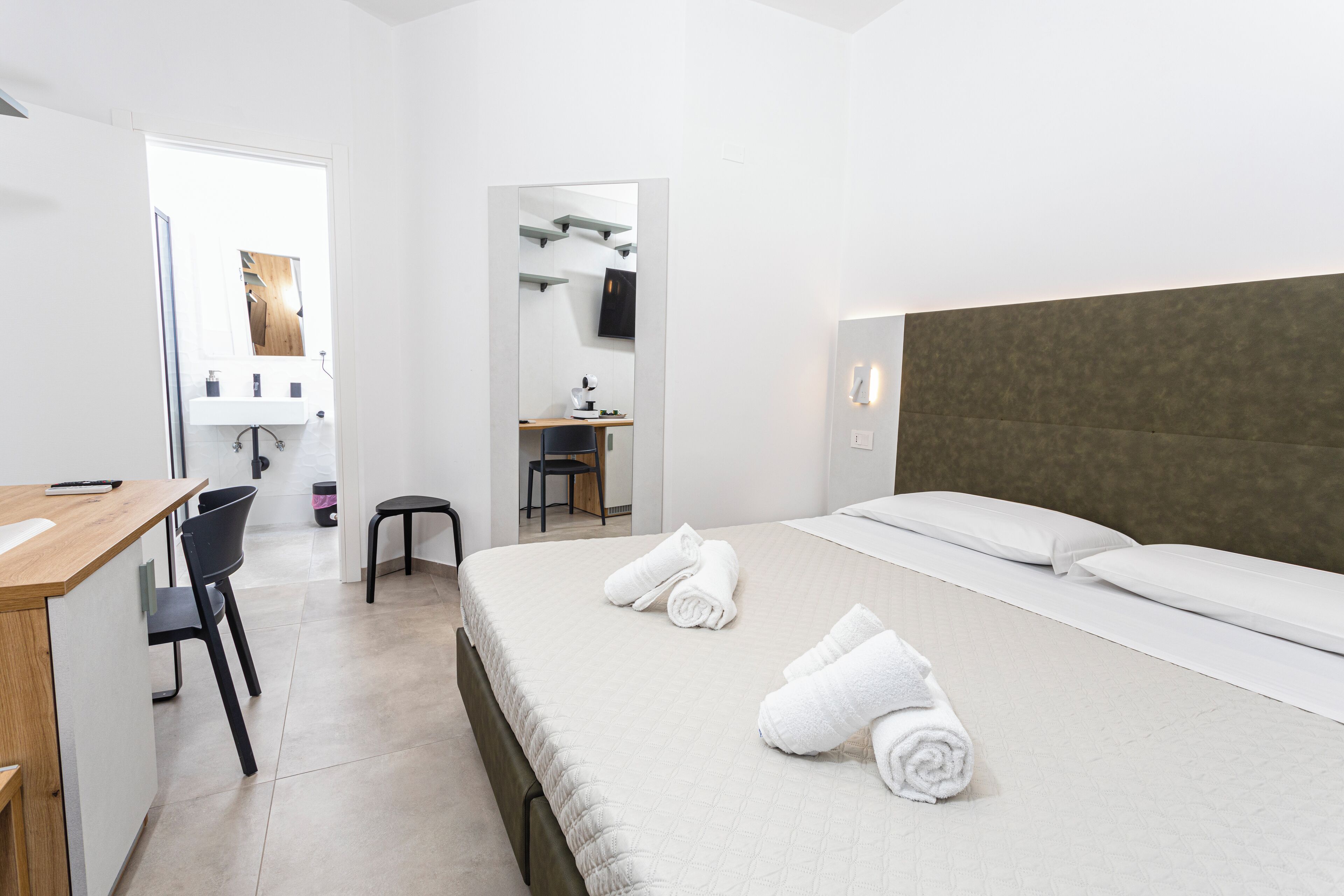 A hotel room with a bed, a desk, a chair, and a mirror.