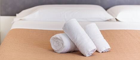 A neatly made bed with white linens and two rolled towels on a textured brown bedspread.