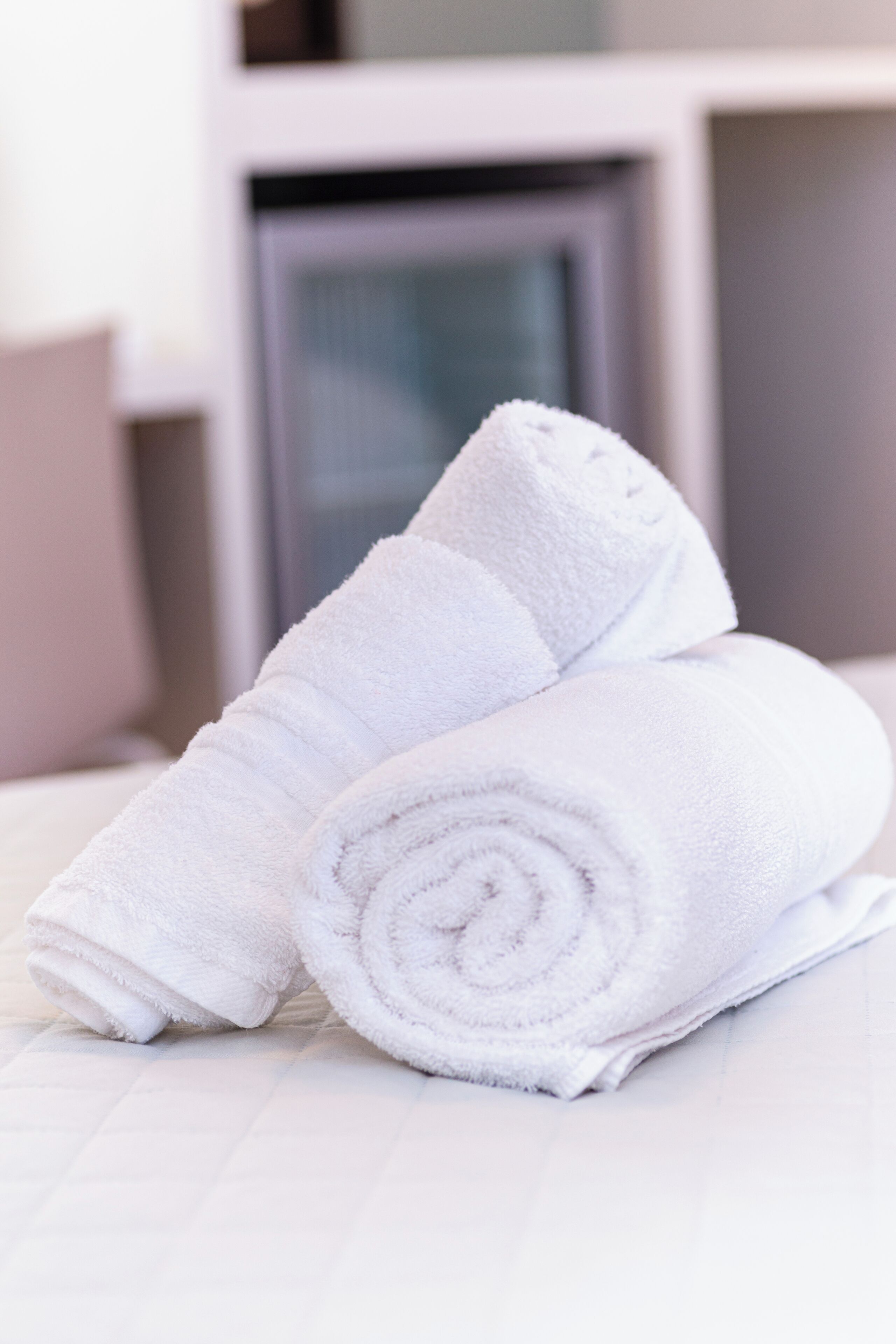 Two neatly rolled white towels on a white bed in a room with a modern design.
