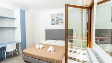 A modern hotel room with a bed, a desk, and a balcony.