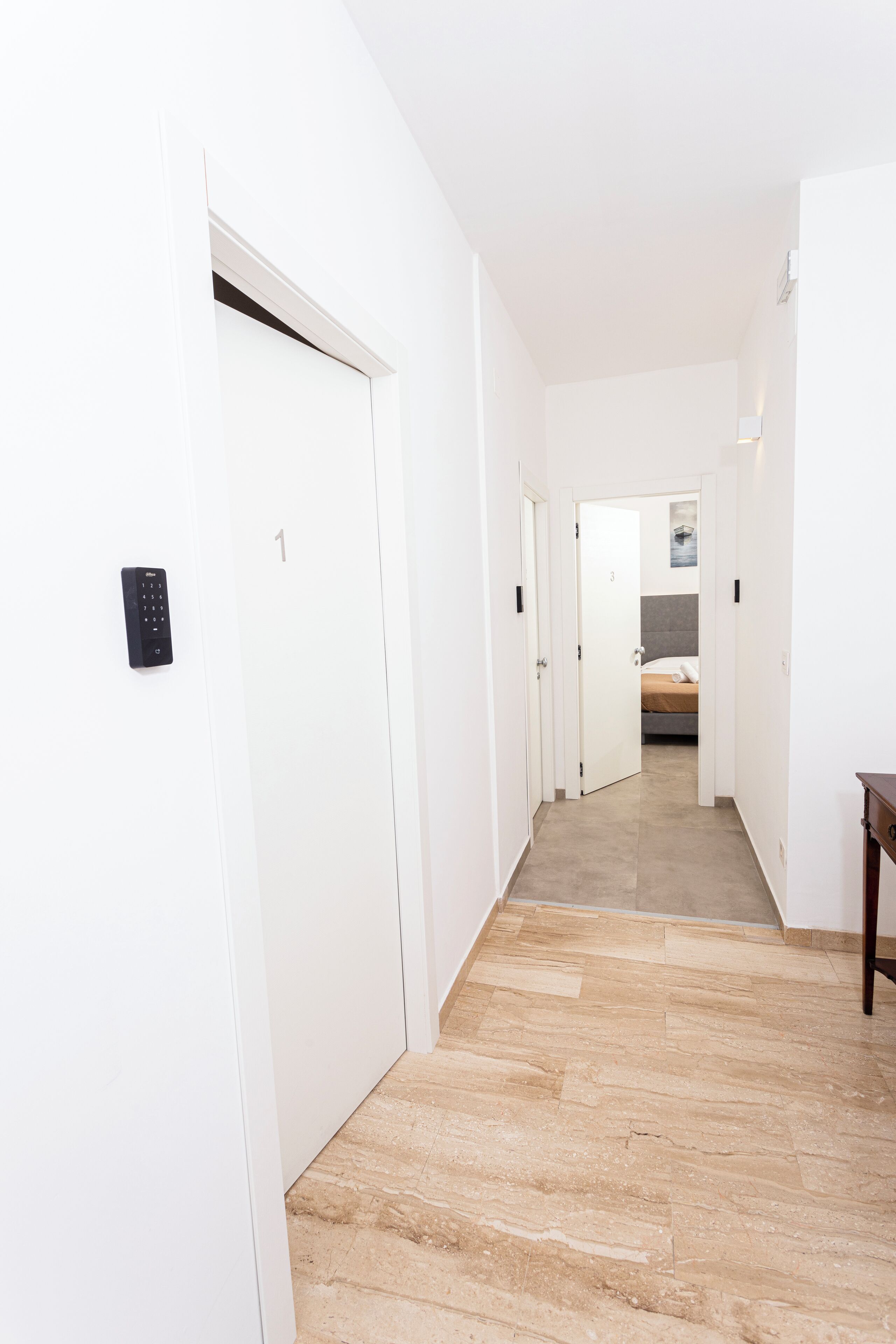 Ein schmaler Flur mit einer Tür, auf der '1' steht, und einem Tastenfeld an der Wand.