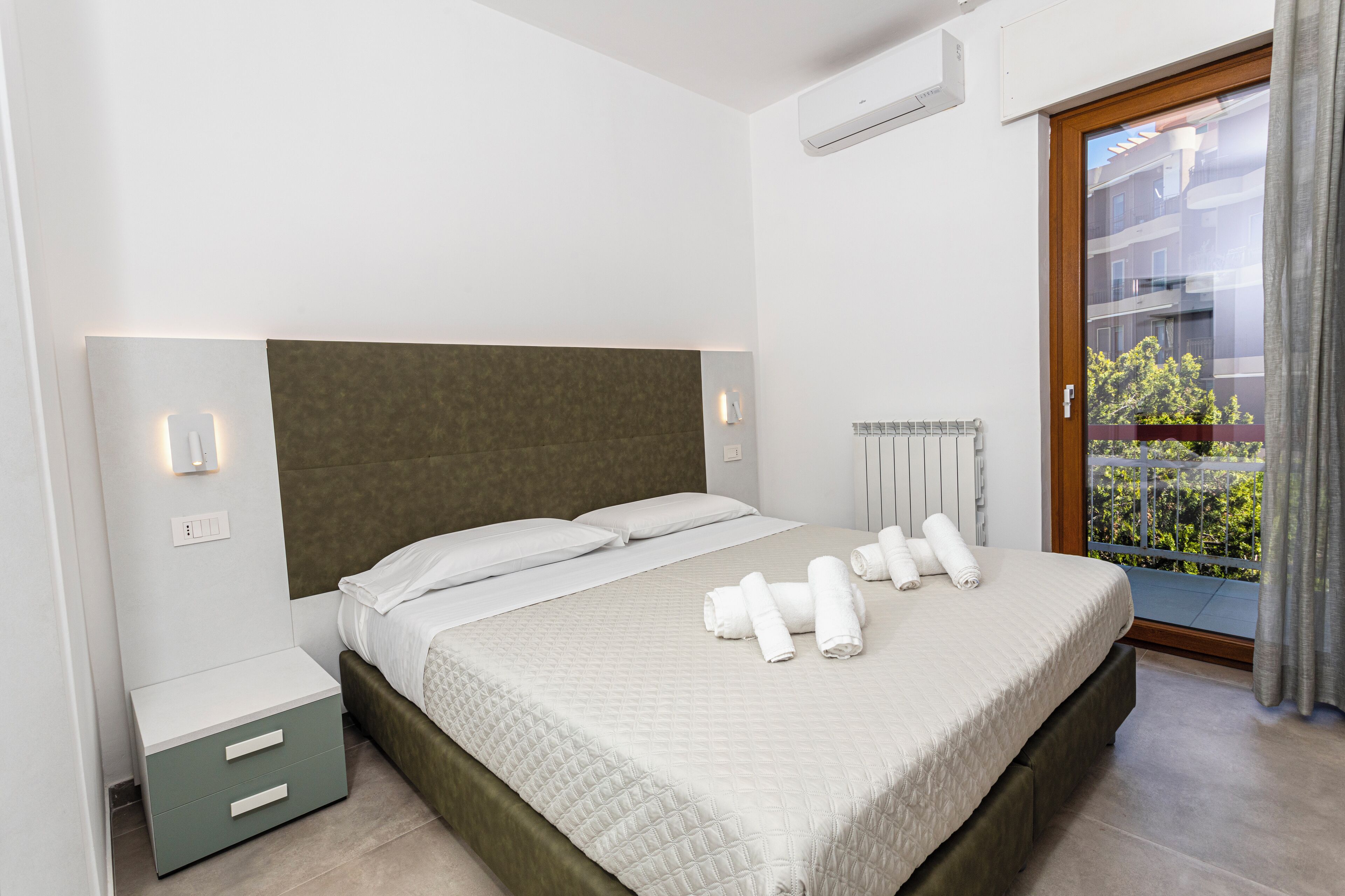 Ein modernes Schlafzimmer mit einem großen Bett, Nachttischen und Blick auf einen Balkon.