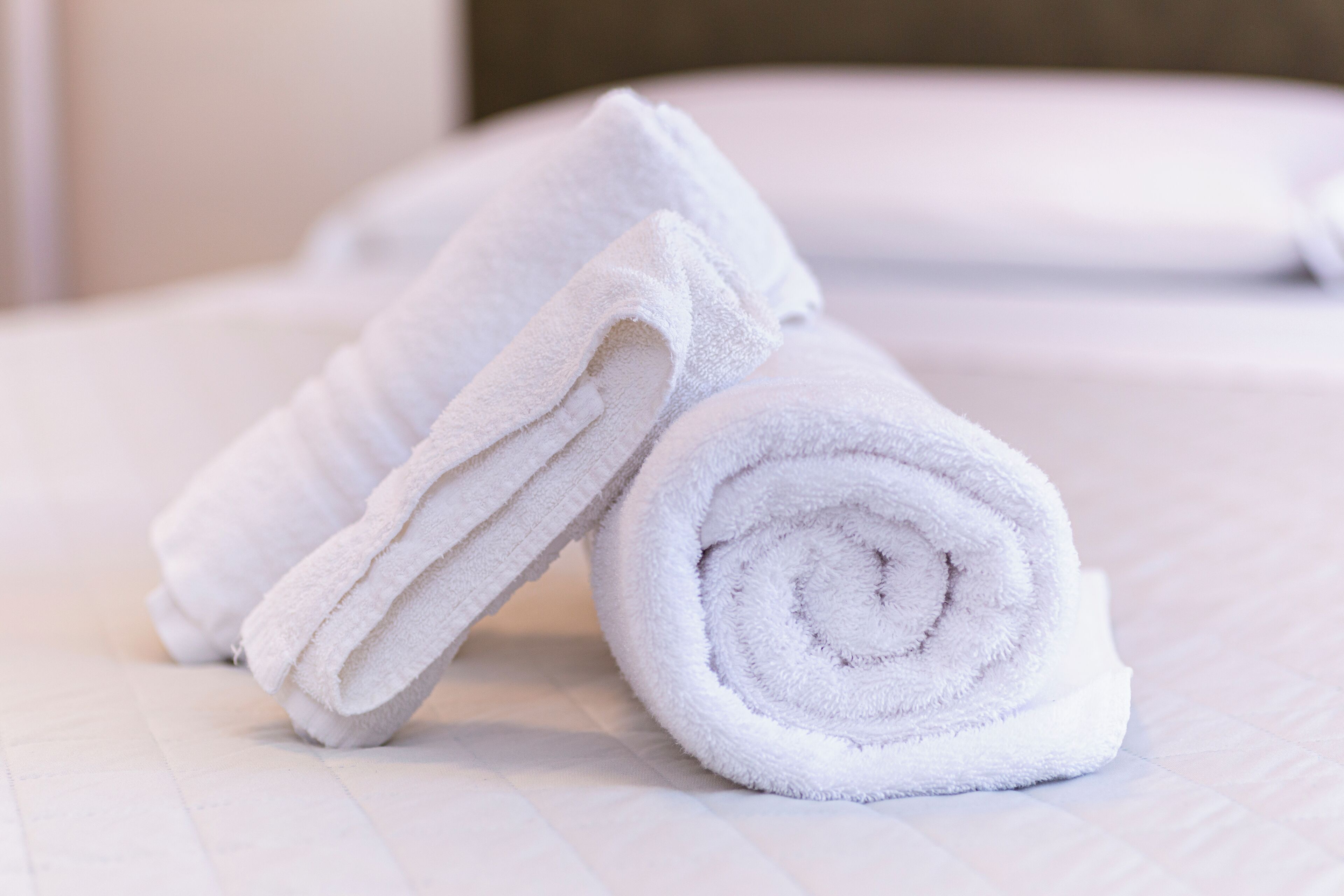 A neatly folded white towel on a bed with a white pillow.