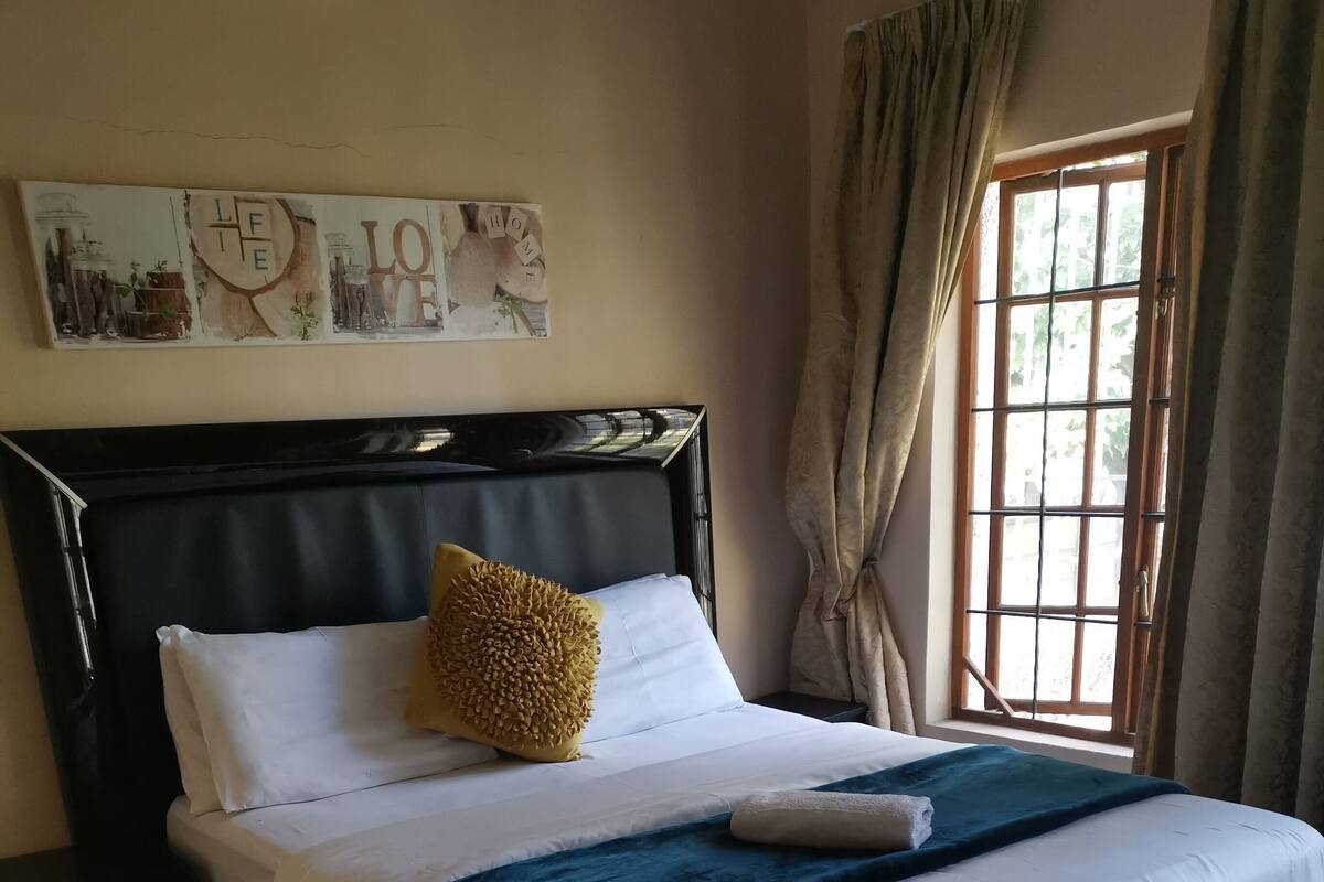 A neatly made bed with white linens and a blue throw, a wooden headboard, and a wall-mounted artwork.