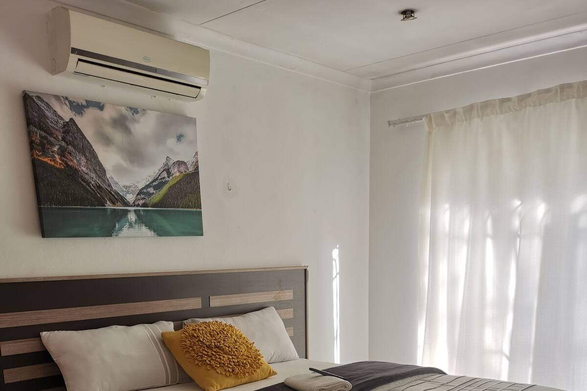 A neatly made bed with a headboard, a bedside table, and a wall-mounted air conditioner.