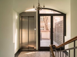 An interior view of a building with an elevator, a staircase with wooden handrails, and a view of the outside through a glass door. - TurnKey | Letna Park Cozy Studio (Praha 7)