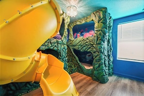 Ein Spielbereich mit Rutsche und Kletterwand, ein Fenster mit Jalousien und eine Deckenleuchte.