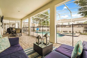 Un espacio exterior techado con zona de estar y vistas a la piscina, una mesa con sillas y una parrilla.