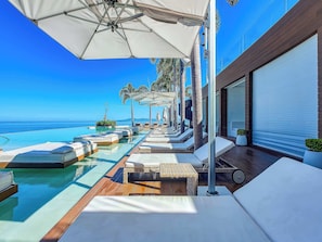 A poolside area with lounge chairs and umbrellas, overlooking a clear blue sea.