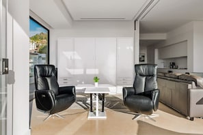 A modern living room with two black leather chairs, a white table, and a view of the city through large windows.