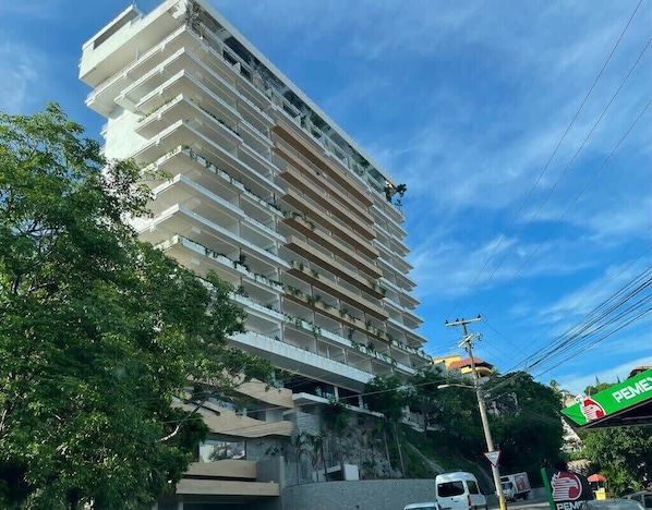 A multi-story hotel with balconies, a visible sign for a PEMEX gas station, and a clear sky.