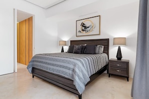 Quarto moderno com cama grande, duas mesas de cabeceira, porta de madeira e uma obra de arte emoldurada na parede.