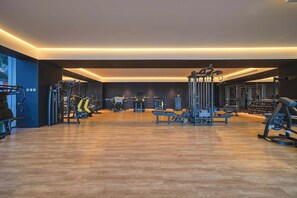A modern gym with various exercise equipment, wooden flooring, and a spacious layout.