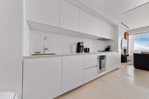 Eine moderne Küche mit weißen Schränken, einer Edelstahl-Spüle, einer Kaffeemaschine und einem Einbauofen.