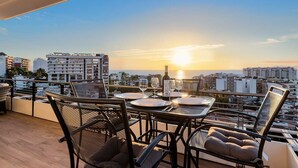 Terraza en la azotea con una mesa lista para cenar, con vistas a un paisaje urbano al atardecer.