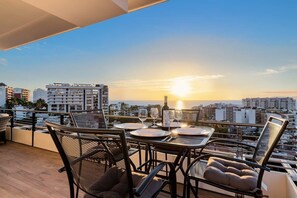 Terraza en la azotea con una mesa lista para cenar, con vistas a un paisaje urbano al atardecer.
