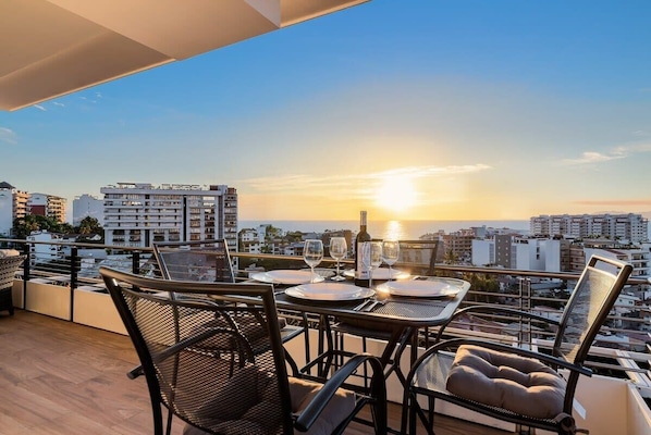 Une terrasse sur le toit, avec une table dressée pour le dîner, d’où l’on peut admirer le panorama urbain au coucher du soleil.