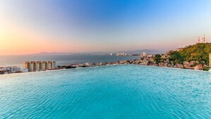 Un paisaje urbano costero con una gran piscina pública, edificios y una vista distante del mar.
