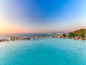 Un paisaje urbano costero con una gran piscina pública, edificios y una vista distante del mar.