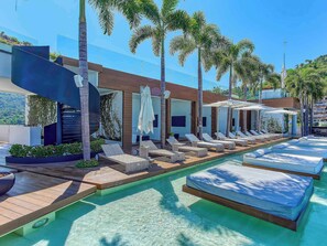 Uma área moderna junto à piscina, com espreguiçadeiras e piscina transparente.