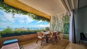 Un balcon avec une table et des chaises en bois, un banc et une vue sur la mer.