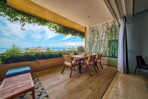 Un balcon avec une table et des chaises en bois, un banc et une vue sur la mer.