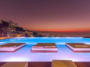 Ein Poolbereich mit Liegestühlen und Blick auf den Ozean bei Sonnenuntergang.