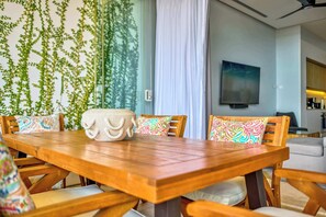 A wooden dining table with colorful cushions, a stone sculpture, and a television on the wall. - Luxury ocean-view condo at SOHO (Puerto Vallarta)