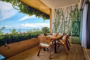 A balcony with a wooden table and chairs, a view of the city, and a wall with hanging plants.