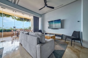 A modern living room with a grey sofa, a wooden coffee table, and a TV mounted on the wall. - Luxury ocean-view condo at SOHO (Puerto Vallarta)