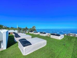 A rooftop terrace with white modular sofas and black cushions, overlooking a coastal cityscape. - Luxury ocean-view condo at SOHO (Puerto Vallarta)