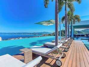 A poolside area with lounge chairs, a wooden deck, and a view of the sea and distant buildings. - Luxury ocean-view condo at SOHO (Puerto Vallarta)