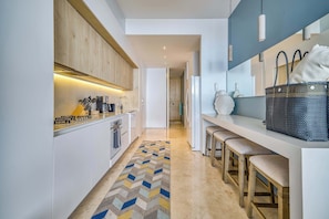 A modern kitchen with a wooden cabinet, a patterned rug, and a bar area with stools. - Luxury ocean-view condo at SOHO (Puerto Vallarta)