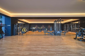 A modern gym with various exercise equipment, wooden flooring, and a spacious layout.